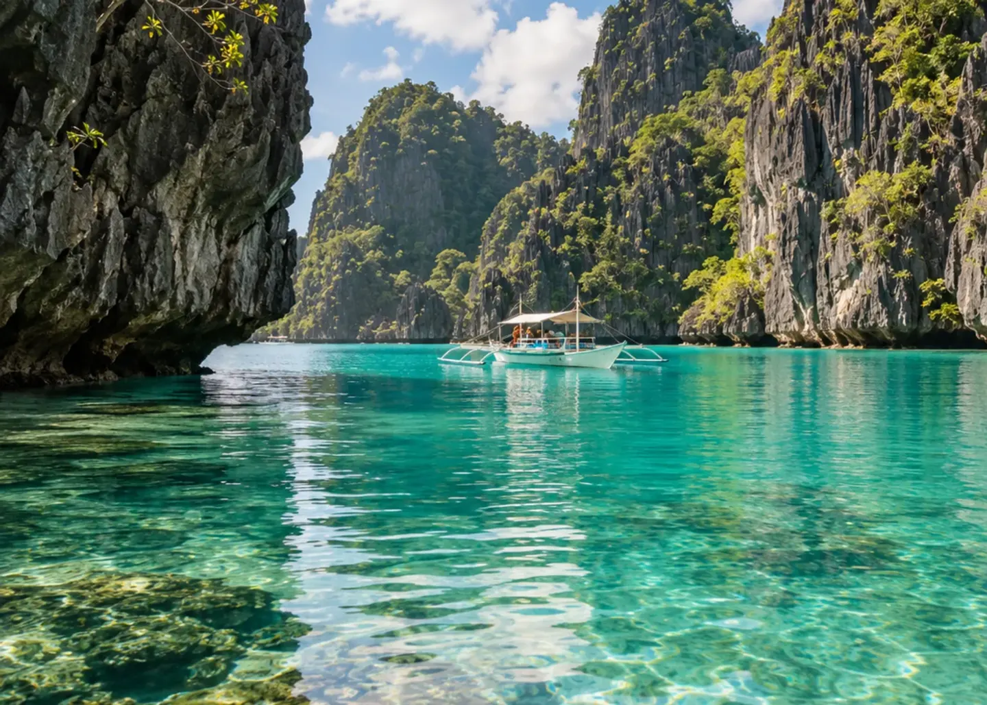 A bangka floating on clear lagoon water beneath towering limestone cliffs.